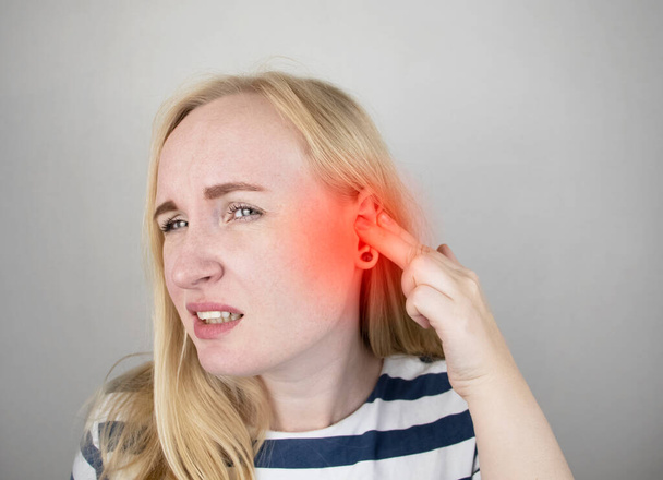 Una mujer sufre de dolor de oído. El meato auditivo duele debido a otitis media, tapón de cerumen, forúnculo del oído o neuralgia del trigémino.
 - Foto, imagen