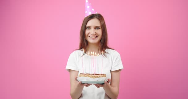 Happy girl in birthday cap holding cake with burning candles - Imágenes, Vídeo