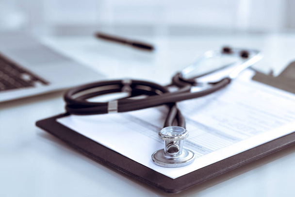 Stethoscope lying at the desk with medical history records and laptop computer. Medicine doctors working table concept - 写真・画像