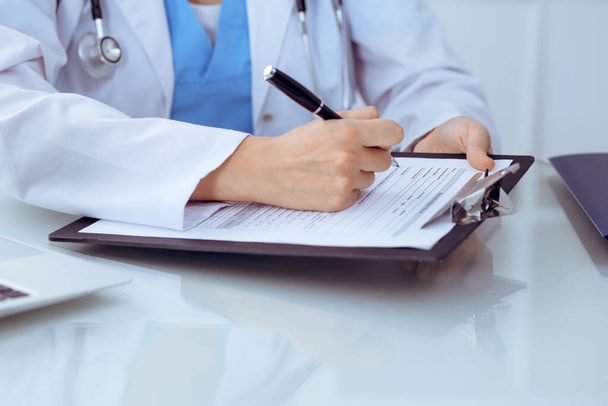 Doctor woman filling up medical form while sitting at the table, close-up of hands - Foto, imagen