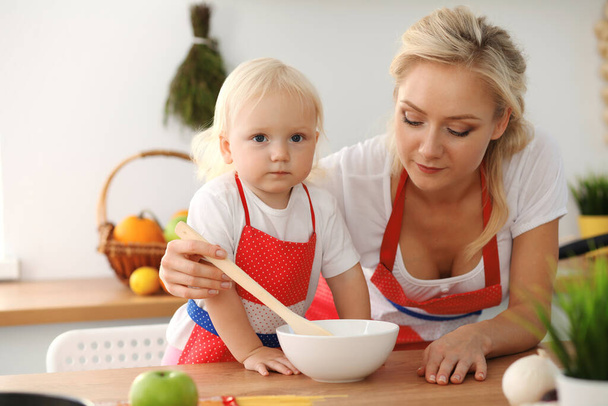 Happy mother and little daughter cooking in kitchen. Spending time all together, family fun concept - Фото, изображение