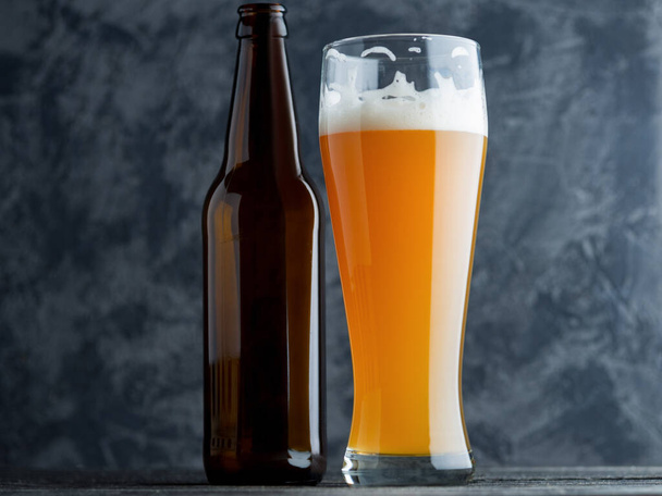 A glass of wheat unfiltered beer on a dark table and a beer bottle - Photo, image