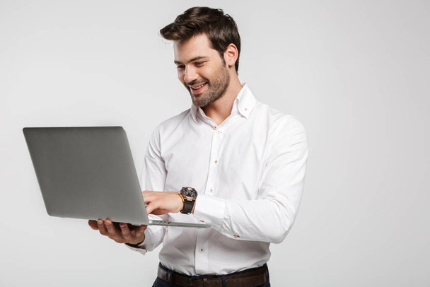 Image of young cheerful businessman in wristwatch holding and using laptop isolated over white background - Photo, Image