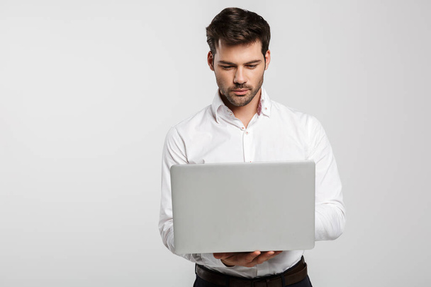 Image of young successful businessman holding and using laptop isolated over white background - Valokuva, kuva