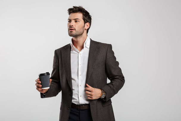 Image of young successful businessman in jacket drinking coffee takeaway isolated over white background - Фото, зображення