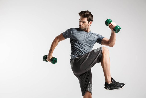 Confident young sportsman exercising with dumbbells isolated over gray background - Foto, Imagem