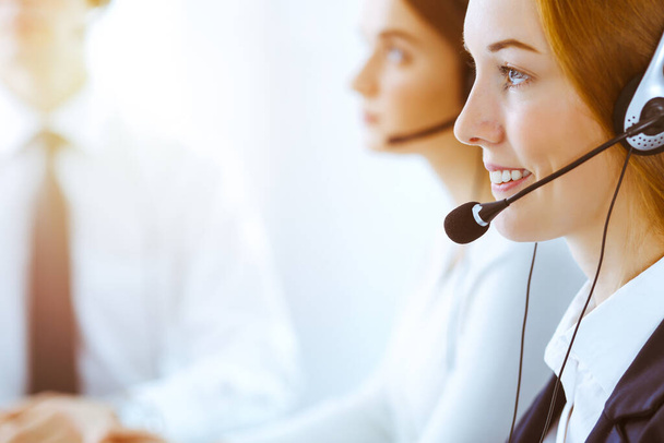 Group of diverse phone operators at work in sunny office. Handsome business woman with headphones consulting clients. Call center and business people concept - Fotografie, Obrázek