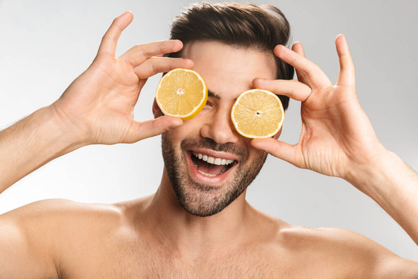 Photo of cheerful half-naked man laughing and making fun with lemon isolated over white background - Фото, изображение