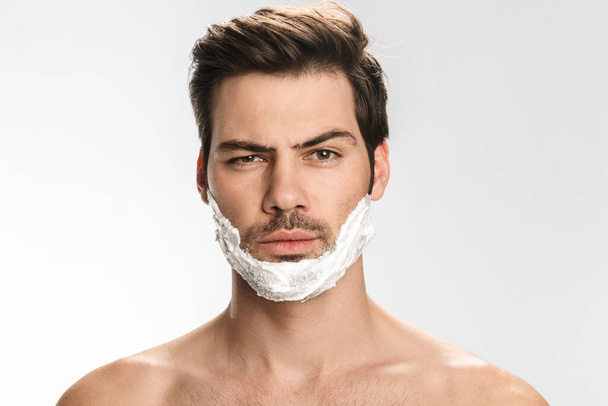Photo of brutal half-naked man with shaving foam on his face isolated over white background - Foto, immagini