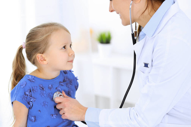 Doctor examining a little girl by stethoscope. Happy smiling child patient at usual medical inspection. Medicine and healthcare concepts - 写真・画像