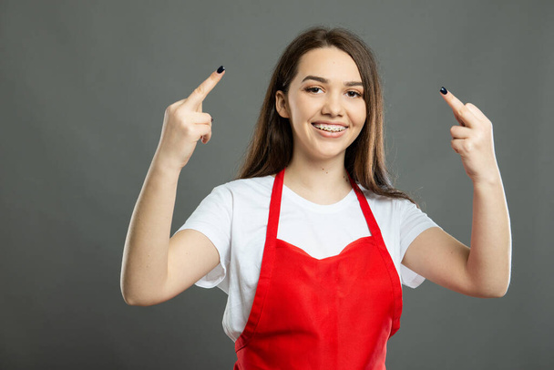 Portret młodej pracowniczki supermarketu pokazującej podwójny obsceniczny gest na szarym tle z przestrzenią reklamową kopiarki - Zdjęcie, obraz