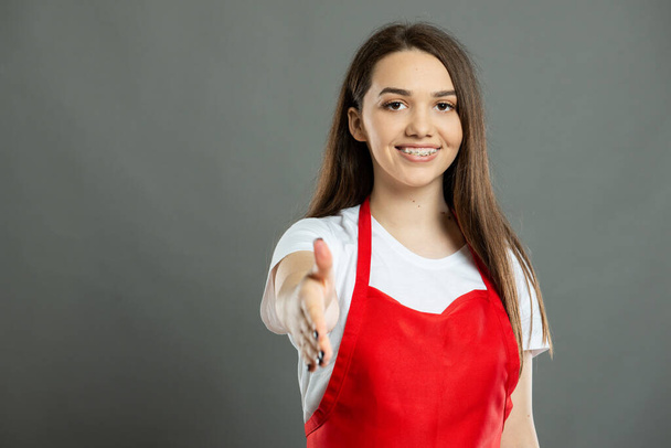 Portrait de jeune employée d'un supermarché offrant une poignée de main sur fond gris avec espace publicitaire pour copier - Photo, image