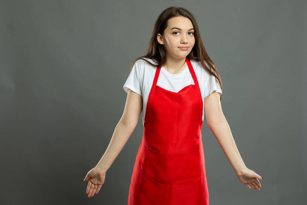 Retrato de jovem atraente funcionário do supermercado feminino fazendo gesto confuso em fundo cinza com espaço de cópia área de publicidade
 - Foto, Imagem
