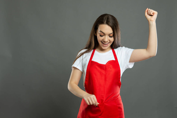 Portrait of young female supermarket employee holding full pockets on gray background with copy space advertising area - Photo, Image