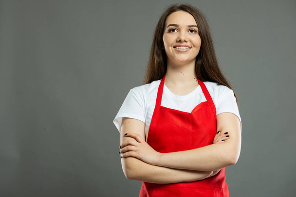 Low angle of female supermarket employee standing with arms crossed on gray background with copy space advertising area - Photo, Image
