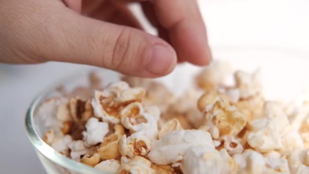 female hand selects delicious fried popcorn from a large glass bowl, the concept of sweets, anticipation of interesting, exciting events - Footage, Video