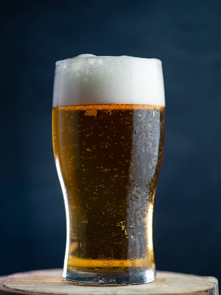 Ένα ποτήρι μπύρα λάγκερ σε σκούρο φόντο. - Φωτογραφία, εικόνα
