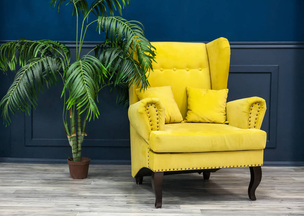 Stylowy żółty fotel na niebiesko-drewnianej ścianie. Stylowe krzesło na tle ściany, palma, modne wnętrze - Zdjęcie, obraz