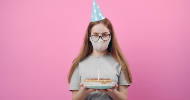 Girl in medical mask and festive cap holding birthday cake - Imágenes, Vídeo