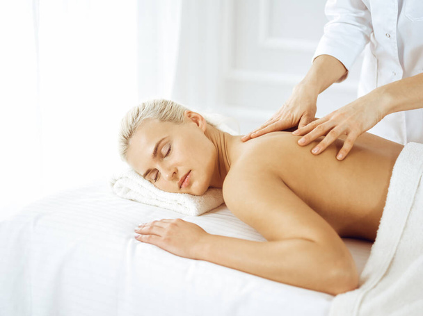 Beautiful blonde woman enjoying back massage with closed eyes. Spa salon concept - Fotografie, Obrázek