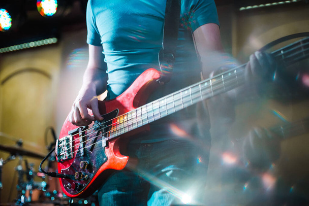 Музыкант играет на бас-гитаре на сцене. Гитара шеи крупным планом на концерте рок-музыки в руках музыканта. Пальцы на ладони. Гитара шеи крупным планом на концерте рок-музыки в руках музыканта. Пальцы на доске
 - Фото, изображение