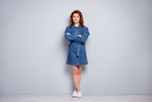 Full length photo of attractive curly lady arms crossed toothy beaming smiling look side empty space wear casual blue denim short dress white shoes isolated grey color background - Foto, Imagem