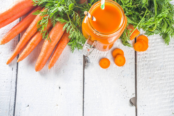 Frullato di carota arancio disintossicante sano o succo di frutta in barattolo di muratore su sfondo bianco in legno con mazzetto di carota fresca. Frullato vegano di verdure. - Foto, immagini