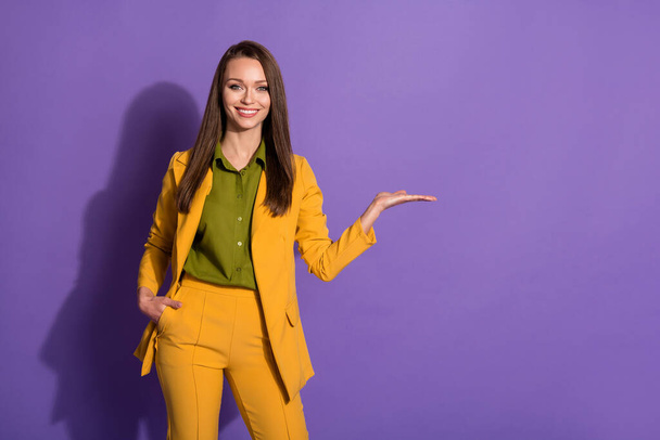 Photo of attractive business lady hold open arm advertising novelty product successful wear yellow luxury office blazer trousers suit blouse shirt isolated purple pastel color background - Photo, Image