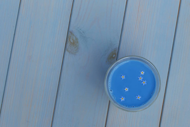 Голубой маття латте из якорь с забудками в стеклянной чашке, стоящий на синем деревянном столе
 - Фото, изображение