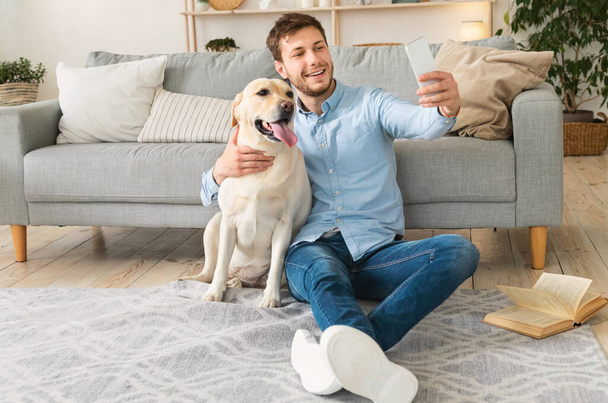 Young man with his dog taking selfie at home - Фото, изображение
