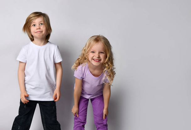 Little blonde girl in purple t-shirt and pants and boy in black and white casual clothes. They smiling, posing isolated on white - Photo, Image
