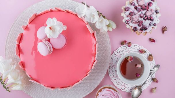 マカロンで装飾された鏡釉のピンクムースケーキ、ピンクの休日の背景に幸せな誕生日のための花。お祝いのケーキよ。トップビュー、フラットレイアウト - 写真・画像