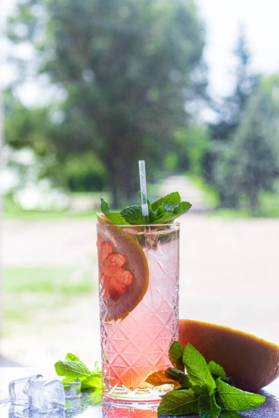 A refreshing summer cocktail with a slice of grapefruit. Alcoholic drink Paloma. Decorated with a sprig of mint and ice cubes. Foreground. - Photo, Image