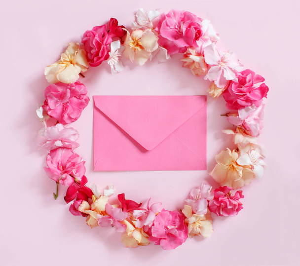 Rosafarbener Umschlag in einem Rahmen aus rosafarbenen Blumen über einem rosafarbenen Hintergrund - Foto, Bild