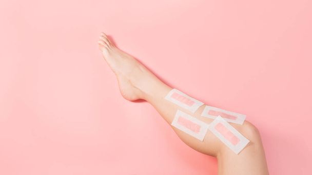 Female depilate legs with pink wax stripes against pink colored background. Removal hair. Minimalism. Top view. Body hygiene, spa procedures banner - Photo, image