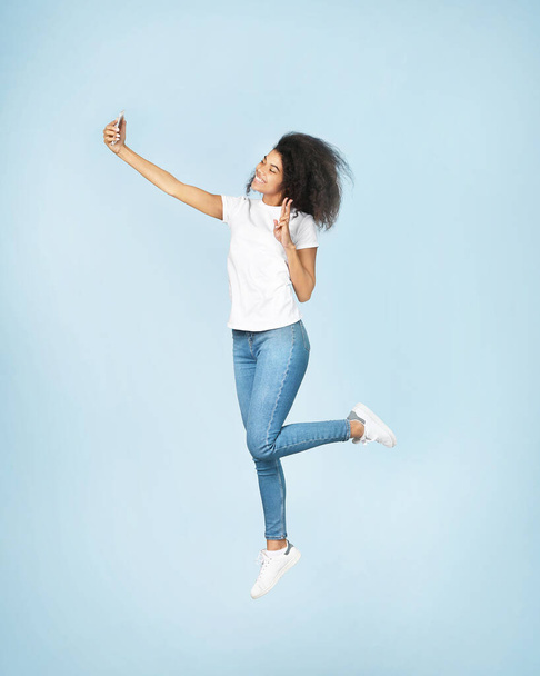 Beautiful african woman jumping on blue background - Фото, зображення