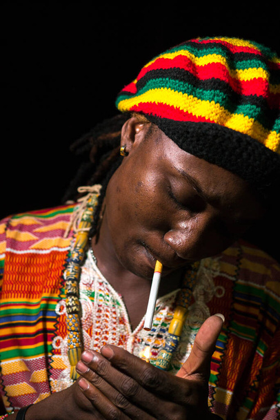 Rosto do jovem africano Rastafarian homem acendendo cigarro ao ar livre à noite
 - Foto, Imagem