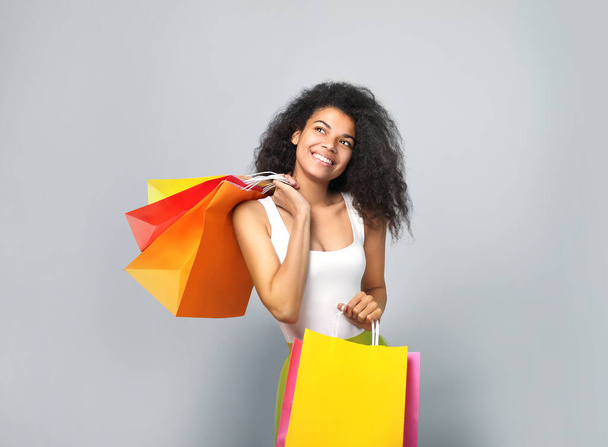 Portrait of a beautiful african woman with shopping bags on grey background - Foto, Bild