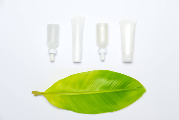 Ficus elastica leaf with skin serum bottles and cream tube  isolated on white backdrop. Organic tropical herb, eco product skin care. Clipping path - Photo, Image