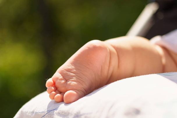 Een pasgeboren baby baadt in de zon. Gezondheid, behandeling, dermatologie, kindertijd, zomer, rust, wandelingen. Kleine baby voet. De pasgeborene slaapt buiten bij warm glanzend weer. Luchtbaden. Kopieerruimte - Foto, afbeelding