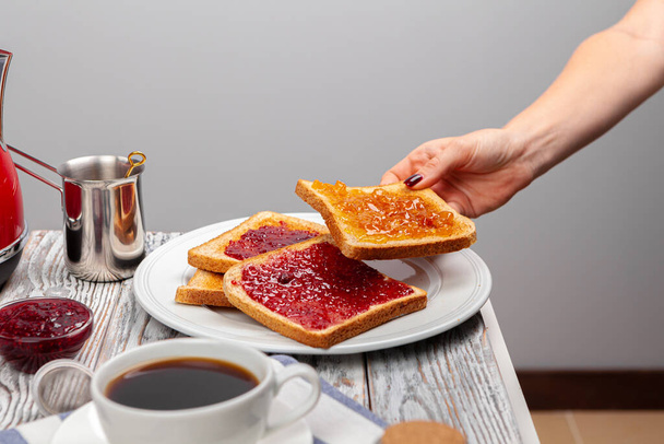 Female hands preparing toasts with fruit jam - Фото, изображение