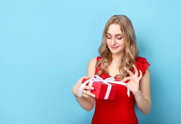 Beautiful woman holding gift on blue background - 写真・画像