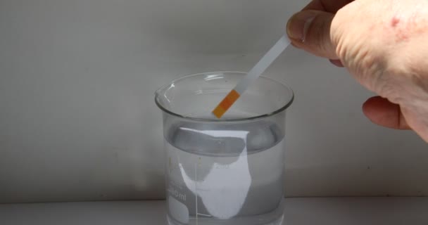 Hand dompelt een teststrip in een oplossing in een bekerglas en detecteert de verkleuring voor analyse - Video