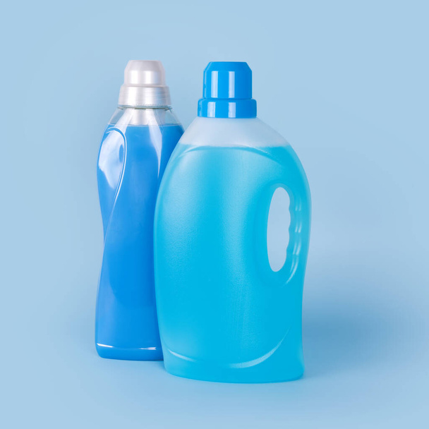 Пляшки миючого засобу та пом'якшувач тканини на синьому фоні. Контейнери для чищення продуктів, побутової хімії. Рідкий пральний порошок і кондиціонер. Концепція прання, прання та прибирання
 - Фото, зображення