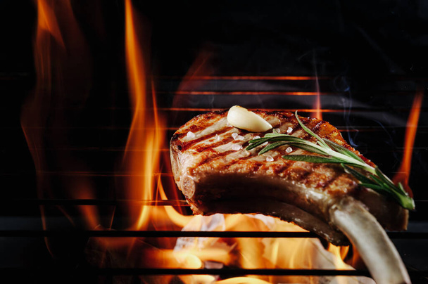 gebratenes Steak zusammen mit gegrilltem und gegrilltem Knoblauch mit Flammenzungen. Auf schwarzem Hintergrund ist die Sicht nicht sonderlich gut - Foto, Bild