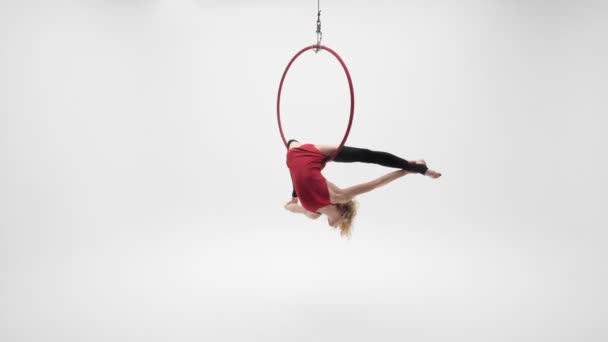 Flexible hübsche blonde Mädchen in einem roten Kleid und schwarzen Strümpfen führt akrobatische Elemente in einem Air Hoop, weiße Cyclorama-Location. - Filmmaterial, Video