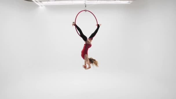 Flexible pretty blonde girl in a red dress and black stockings performs acrobatic elements in an air hoop,white cyclorama location. - Metraje, vídeo