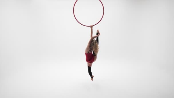 Flexible pretty blonde girl in a red dress and black stockings performs acrobatic elements in an air hoop,white cyclorama location. - Video, Çekim