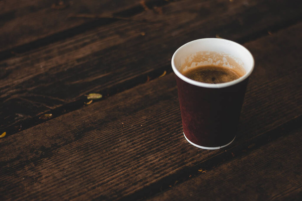 日中は濃い木製の表面に泡が配置されたコーヒーの小さな茶色のカップ朝食のための午前中に熱くて甘い飲み物 - 写真・画像