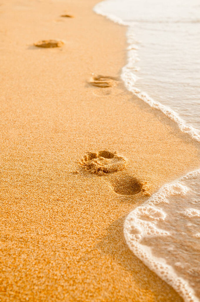 Ślady stóp na piasku o zachodzie słońca. Piękna piaszczysta plaża tropikalna z falami morskimi. Kroki na brzegu. - Zdjęcie, obraz